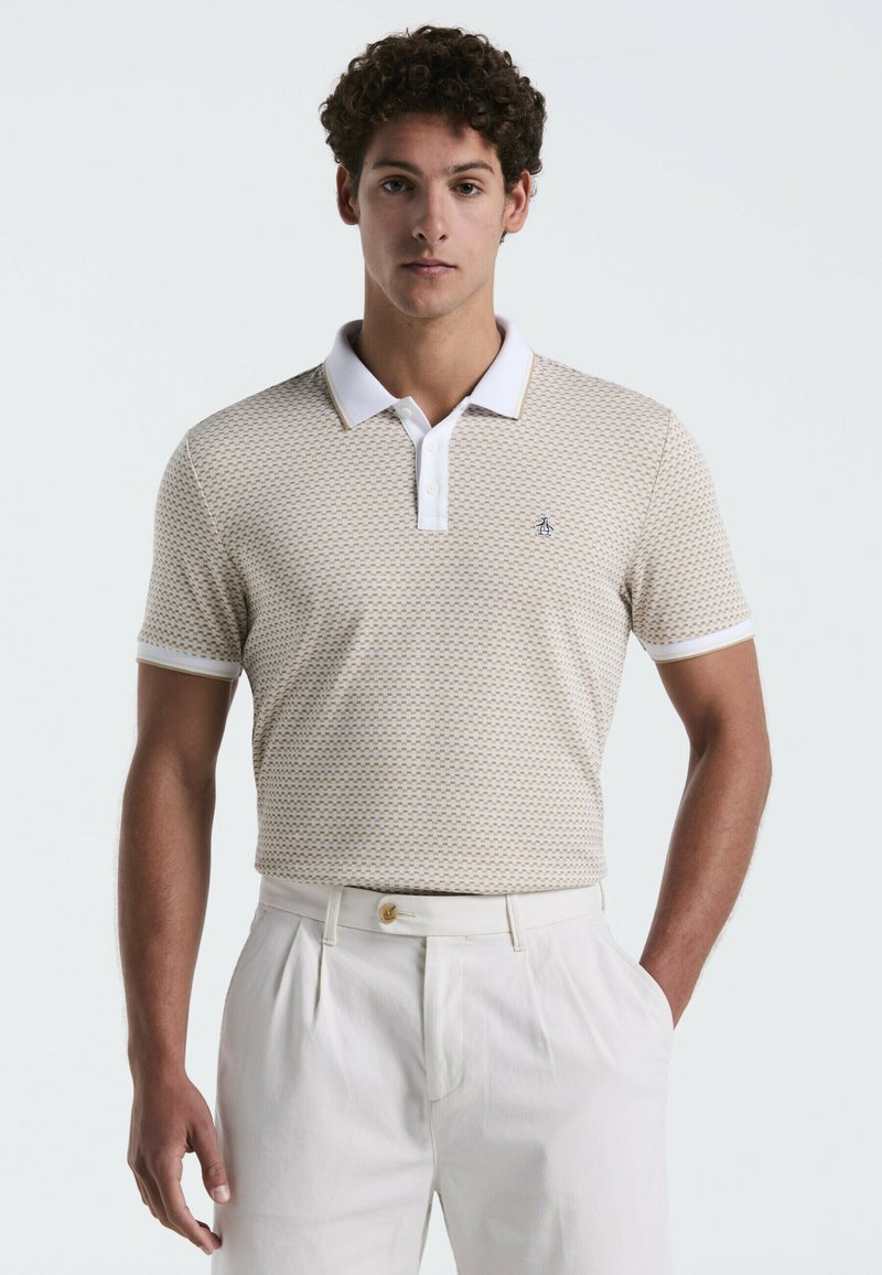 Kurzärmliges Polohemd in Hellbeige mit geometrischem Muster, kontrastierendem weißen Kragen und Logo-Detail auf der Brust, kombiniert mit weißen Hosen.