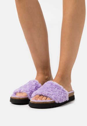 Sandales glissantes moelleuses violettes avec des larges sangles, semelle intermédiaire en liège et semelle en caoutchouc noir texturé. orteils découverts visibles. Finition en tissu doux.