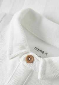 Polo bianco con un motivo a spina di pesce testurizzato, colletto classico e dettaglio del bottone marrone sul patta.