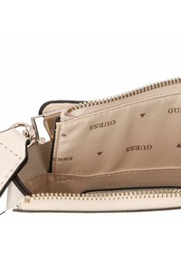 Intérieur de sac à main couleur crème avec une doublure en tissu lisse présentant un motif de logo répété. Fermeture éclair et détails en métal.