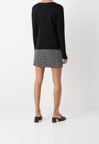 Svart långärmad tröja i kombination med en kort kjol med svart-vitt houndstooth-mönster, kompletterad med svarta klackskor med blockklack.