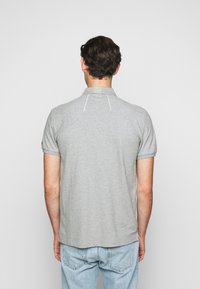 Šedé polo tričko s krátkým rukávem, vroubkovaným límečkem a malými detaily na zadní straně. Kombinováno se světle modrými džínami.