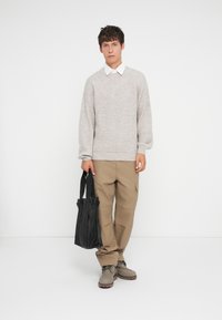 Light gray knit sweater, beige cargo pants, gray shoes, and a black tote bag. Simple design with a textured finish and contrasting colors.