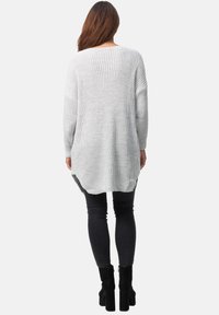 Suéter de punto gris claro de manga larga con un corte holgado, que presenta aberturas laterales y un dobladillo curvado, combinado con jeans negros ajustados y botas de tobillo.