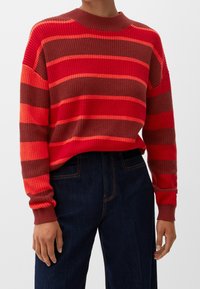 Gestreifter Strickpullover in Rot und Orange mit Rundhalsausschnitt, strukturiertem Stoff und langen Ärmeln. Kombiniert mit dunklen Jeans.