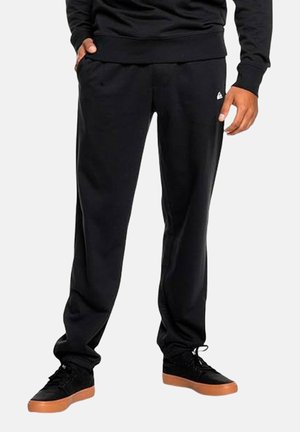 Pantalones de chándal negros con cintura elástica, bolsillos laterales y un pequeño detalle de logo. Fabricados en una tela suave, con una silueta ajustada y una textura lisa.