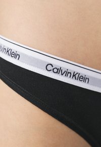 Črne bombažne hlačke z belo elastično pasom, na katerem je napis "Calvin Klein". Gladka tekstura, udoben oprijem in preprost dizajn.