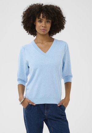 Lichtblauwe gebreide trui met een V-hals, driekwart mouwen en geribbelde manchetten. Zachte textuur, gecombineerd met donkere spijkerbroek.