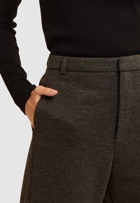 Pantalon ajusté gris foncé en tissu texturé, avec des poches latérales et un devant plat. Assorti à un haut noir à manches longues ajusté.