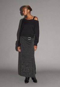 Svart off-shoulder-tröja kombinerad med en lång, mörkgrå glittrig kjol, som har en slits på sidan och en stor metallisk spännare. Svarta ankelskor.