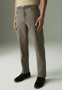 Jeans in denim grigio con una vestibilità raffinata, dotati di cinque tasche, chiusura con zip e una finitura leggermente scolorita, abbinati a scarpe nero con lacci.