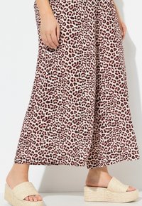 Weite Hose mit einem rosa Leopardenmuster, kombiniert mit beigen Keilabsatzsandalen mit gewebter Textur und offener Zehe.