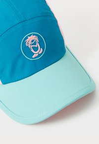 Krāsains cepures bloks, kuram ir tirkīza, rozā un piparmētru zaļas krāsas audums, ar apļa izšuvumu priekšpusē.