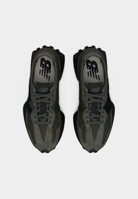 Ζευγάρι σκούρα πράσινα και μαύρα αθλητικά παπούτσια New Balance, φαίνονται από πάνω σε λευκό φόντο, εμφανίζοντας τα κορδόνια και το λογότυπο στο εσωτερικό.