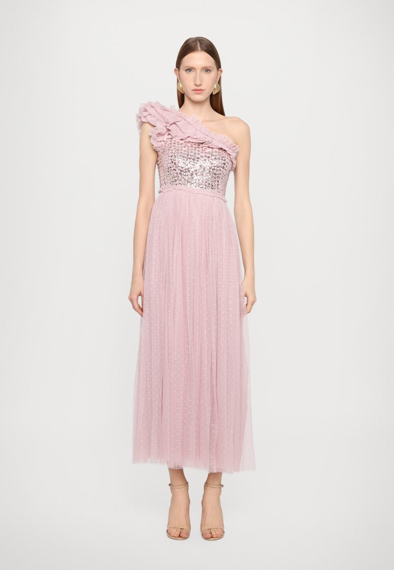 Rosa Tüllkleid mit einem Schulter-Rüschendetail, einem paillettenbesetzten Oberteil und einem bodenlangen Rock mit strukturierten Punkten. Schlichte, hautfarbene Absätze runden den Look ab.