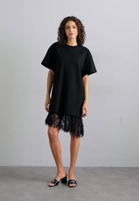Fekete, bő oversized pólóruha rövid ujjakkal, csipkés díszítéssel az alján. Simító anyag és laza fazon, réteges kialakítással.