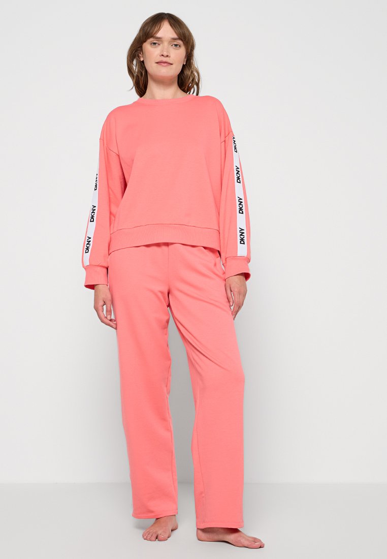 Rosa Sweatshirt mit rundem Halsausschnitt und langen Ärmeln, das kontrastierende weiße Logosstreifen aufweist. Kombiniert mit passenden, lockeren Hosen.