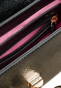 Schwarzes, strukturiertes Innenfutter der Handtasche mit einem pinken Futter, das eine Reißverschlusstasche und ein goldfarbenes Hardware-Verschlusss Detail aufweist.