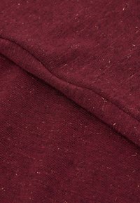 Vínová látka s texturovaným vzhledem a drobnými flíčky. Materiál je měkký, s hladkým, rovnoměrným tkaním a čistými okraji švů.