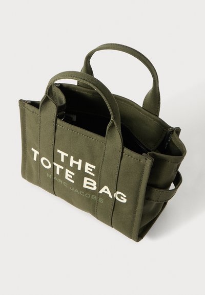 Oliwkowa torba płócienna z podwójnymi uchwytami, z białym napisem "THE TOTE BAG" oraz "MARC JACOBS" z przodu. Zamek błyskawiczny.