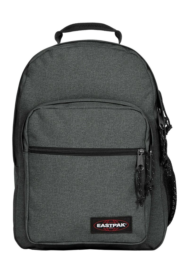 Mochila de tela gris con un compartimento principal con cremallera, un bolsillo frontal con cremallera y un bolsillo de malla lateral. Presenta un parche con el logo y cremalleras duraderas.