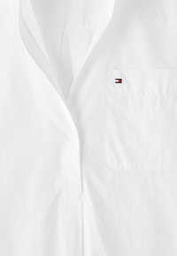 Camicia bianca con colletto, taschino sul petto e un piccolo logo ricamato in rosso, bianco e blu sulla tasca.