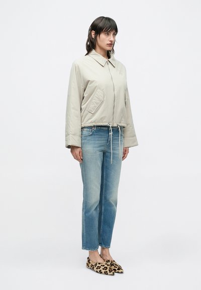 Μπεζ ελαφρύ μπουφάν με γιακά και μπροστινές τσέπες, σε συνδυασμό με ανοιχτό μπλε τζιν με ίσια γραμμή και παπούτσια τύπου slip-on με λεοπάρ φάσα.