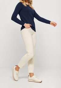 Námořnický svetr s dlouhým rukávem, krémové tapered kalhoty a bílé tenisky s hnědými akcenty. Hladká textura, volný střih a čisté linie.