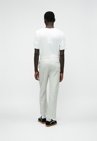 Pantalones de chándal grises con un corte relajado, que cuentan con una cinturilla con cordón y un bolsillo trasero, combinados con una camiseta blanca básica y zapatos negros.