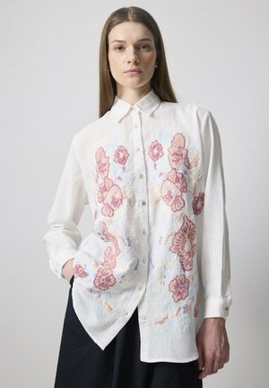 White linen shirt featuring colorful floral embroidery in pink and blue tones, long sleeves, and a button-down front.