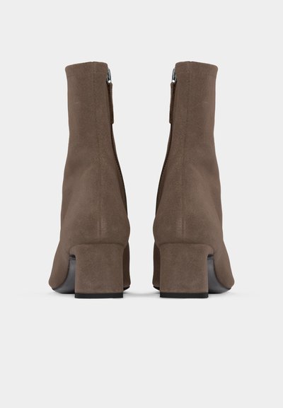 Ζευγάρι καφέ μπότες αστραγάλου από σουέτ με τακούνια block, από πίσω, σε απλό ανοιχτό γκρι φόντο.