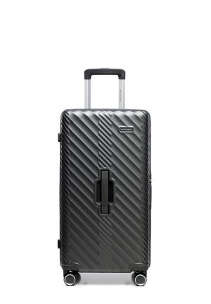 Czarna walizka z twardą skorupą z diagonalnymi rowkami, wysuwanym uchwytem, centralnym uchwytem oraz czterema obrotowymi kółkami, stojąca pionowo na białym tle.
