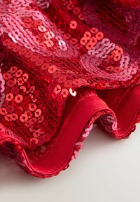 Tessuto rosso con paillettes a motivo ondulato, con paillettes circolari in varie tonalità di rosso, rifinito con un bordo in tessuto rosso liscio.