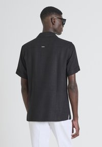 Zwart linnen shirt met korte mouwen en een ontspannen pasvorm. Opvallende kenmerken zijn de gewatteerde kraag en een klein label aan de achterkant.