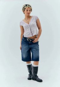 Svetlo vijolična teksturirana kratka majica s volančiči, uparjena z blue jeans hlačami do kolen in črnimi škornji do kolen.