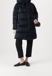 Czarna puchowa kurtka w kratę, z zamkiem błyskawicznym i dużym kapturem. Połączona z czarnymi spodniami 3/4 i płaskimi butami.