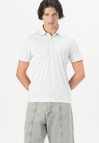 Polo de manga corta en gris claro con un sutil patrón texturizado, cuello abotonado y corte relajado, combinado con pantalones grises de pierna recta.