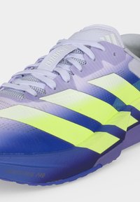 Κοντινό πλάνο μιας μωβ αθλητικής παπούτσας Adidas Drop Set με λευκές και νέον κίτρινες ρίγες και φωτεινή μπλε σόλα, κατασκευασμένη από δίχτυ και συνθετικά υλικά.