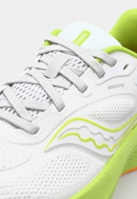 Baskets de course blanches avec des lacets gris, en tissu en maille, avec des accents verts et un motif ondulé blanc sur le côté. Elles présentent un talon spécialement rembourré.