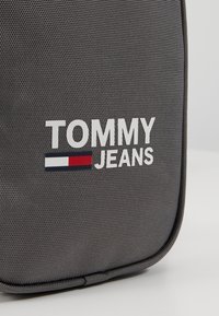 Tessuto grigio testurizzato con logo "TOMMY JEANS" bianco e piccolo emblema rettangolare rosso, bianco e navy sulla superficie della borsa.
