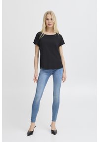 T-shirt nera in cotone con maniche corte arrotolate, abbinata a jeans skinny azzurri e décolleté nere con punta appuntita. Design semplice e casual.