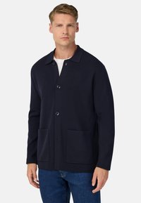 Jūras spēku virsjakas ar apavalka apkakli, priekšējiem pogām un divām priekšējām kabatām. Izgatavota no teksturēta adījuma auduma. Ikdienišķa piegriezuma.