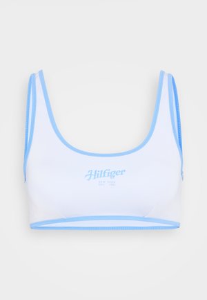 Sutiã desportivo branco com detalhes em azul claro, apresentando um decote em forma de scoop, alças finas e "Hilfiger New York Est. 1985" estampado em azul claro.