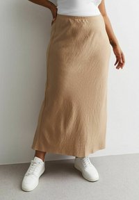Falda beige hasta la rodilla hecha de un tejido texturizado, con un diseño recto y costura lateral. Combinada con zapatillas blancas.