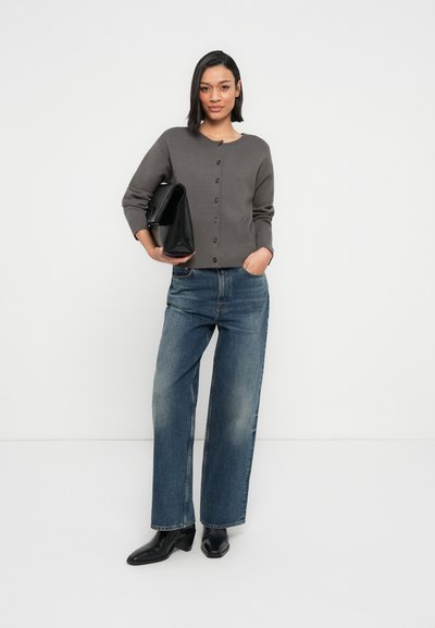 Cardigan gris tricoté avec encolure ronde et boutons devant, associé à un jean bleu délavé à jambes larges et des bottines noires, tenant un sac noir.