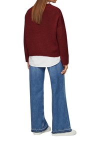 Bordeaux gebreide trui met lange mouwen, een rechte pasvorm en een gestructureerde afwerking, gedragen over een witte blouse en gecombineerd met losse blauwe jeans.