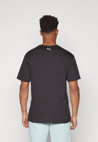 Camiseta de algodón negra con mangas cortas, con cuello redondo y un logo blanco de Puma en la parte superior de la espalda. Textura suave con corte estándar.