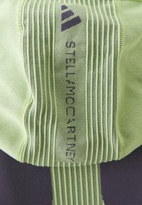 Ljust grönt tyg med vertikal ribbad textur och en central remsa som visar Adidas-logotypen och texten "STELLAMcCARTNEY" i svart.