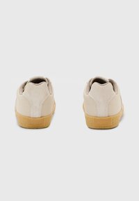 Sneaker mit einem strukturierten beige oberen Material, Wildleder-Akzenten und einer hellbraunen Gummisohle. Mit einem Logo-Tag an der Ferse.