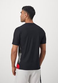 Black short-sleeve athletic shirt with subtle texture, features a gray gradient at sides and red accents at the hem. Round neckline.